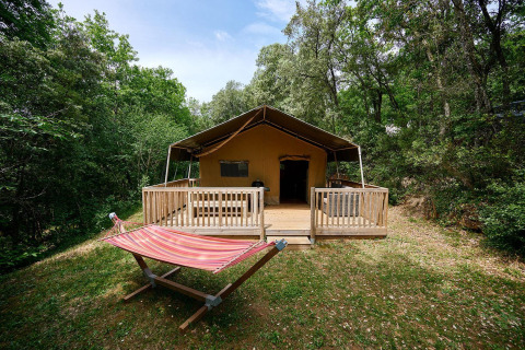 Tienda safari Villatent Wood en el Camping Le Pech Charmant en Francia, rodeada de bosque y hamaca afuera.