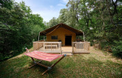 Tienda safari Villatent Wood en el Camping Le Pech Charmant en Francia, rodeada de bosque y hamaca afuera.