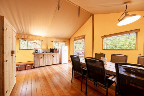 Interior de la tienda safari Villatent Wood en Camping Le Pech Charmant, con comedor y cocina pequeña.