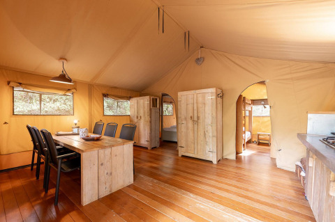 Vista interior de una tienda safari con muebles de madera en Villatent Wood, Camping Le Pech Charmant, Francia.