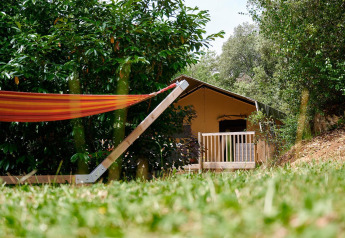 Safari-Zelt Villatent Wood mit Hängematte und Terrasse, umgeben von viel Grün auf Camping Le Pech Charmant.