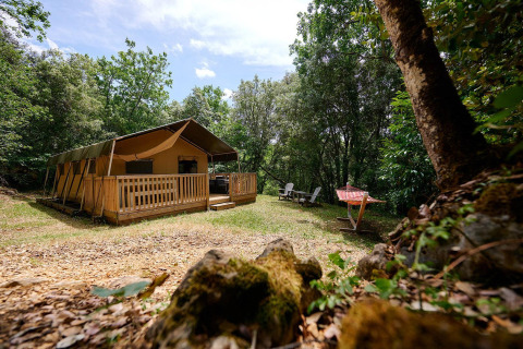 Tienda safari Villatent Wood en Camping Le Pech Charmant, Francia, rodeada de naturaleza y árboles frondosos.