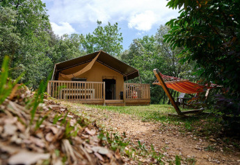 Safari-Zelt Villatent Wood mit Terrasse und Hängematte auf Camping Le Pech Charmant in Frankreich im Wald.