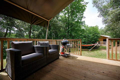 Vista desde la terraza con sofá, barbacoa y hamaca en la naturaleza, en Villatent Wood, Camping Le Pech Charmant.