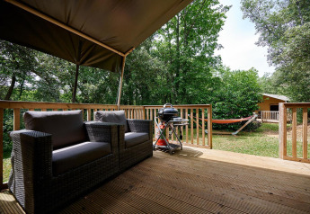 Blick von einer Terrasse mit Sofa, Grill und Hängematte im Grünen bei Villatent Wood, Camping Le Pech Charmant.