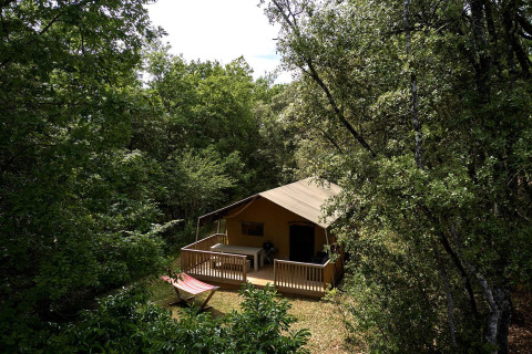 Tienda safari Villatent Wood en Camping Le Pech Charmant, Francia, rodeada de árboles y vegetación.