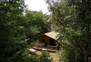 Tienda safari Villatent Wood en Camping Le Pech Charmant, Francia, rodeada de árboles y vegetación.