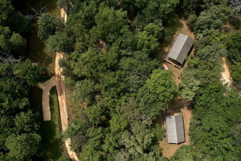 Vista aérea de tiendas safari entre bosques en Camping Le Pech Charmant, Francia, junto a senderos y árboles.