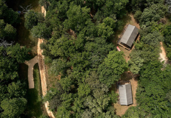 Luftaufnahme von Safarizelten im Wald auf dem Campingplatz Le Pech Charmant in Frankreich neben Wegen.