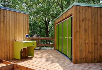 Holzgebäude mit grünen Türen und Waschbecken auf einem Holzdeck bei Villatent Wood, Camping Le Pech Charmant.