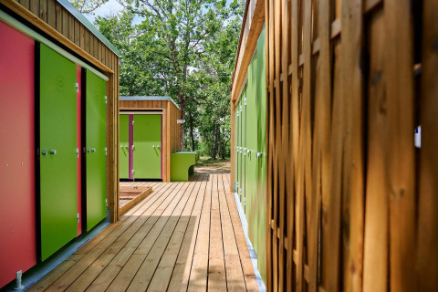 Edificios coloridos y pasarela de madera en Villatent Wood de Camping Le Pech Charmant en Francia.