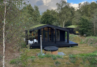 Casa diminuta negra con terraza, jacuzzi y sauna rodeada de vegetación en Wilsumer Berge, Alemania.