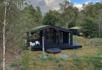 Sort tiny house med terrasse, spabad og sauna omgivet af grønt landskab ved Wilsumer Berge, Tyskland.