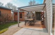 Patio esterno con tavolo da pranzo e sedie sotto pergolato a Veluwelodge XL, Holiday park De Boshoek, Paesi Bassi.