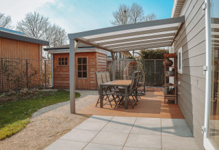 Patio esterno con tavolo da pranzo e sedie sotto pergolato a Veluwelodge XL, Holiday park De Boshoek, Paesi Bassi.