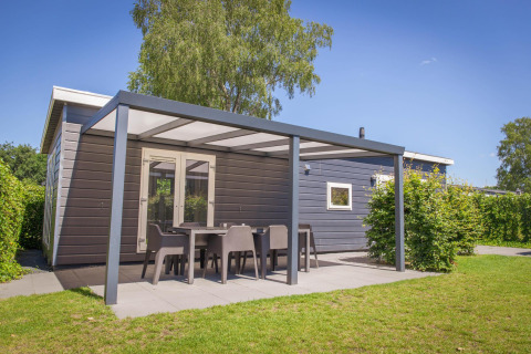 Vue extérieure de la Veluwelodge XL avec terrasse couverte et mobilier de jardin au parc De Boshoek.