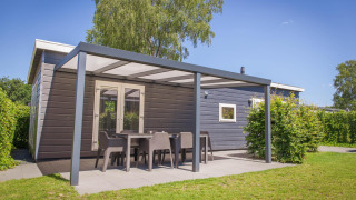 Vue extérieure de la Veluwelodge XL avec terrasse couverte et mobilier de jardin au parc De Boshoek.