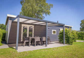 Vue extérieure de la Veluwelodge XL avec terrasse couverte et mobilier de jardin au parc De Boshoek.