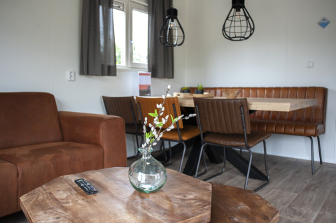 Woonruimte in Veluwelodge XL met bruine leren zitplaatsen, houten tafel en moderne verlichting.