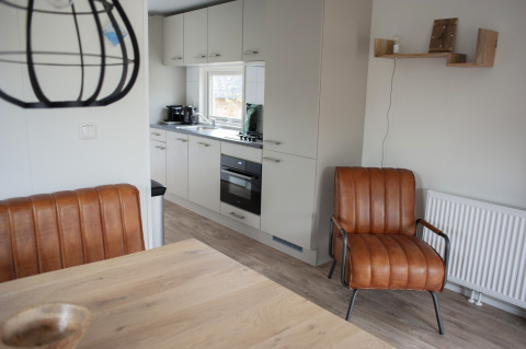 Cocina y sala moderna en Veluwelodge XL, con asientos de cuero, estanterías y ambiente acogedor y luminoso.