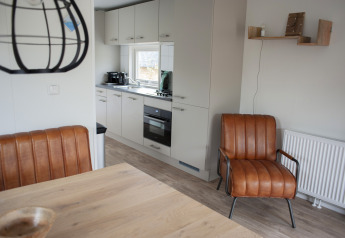 Cocina y sala moderna en Veluwelodge XL, con asientos de cuero, estanterías y ambiente acogedor y luminoso.