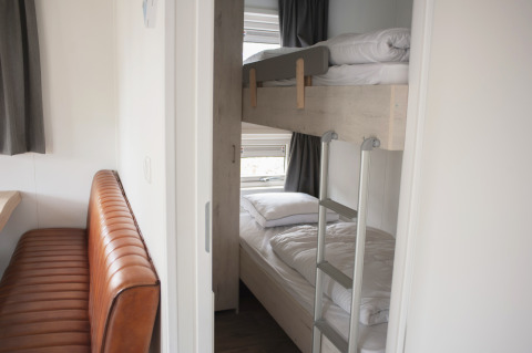 Interieur met stapelbedden en bruine bank in Veluwelodge XL bij Vakantiepark De Boshoek, Nederland.