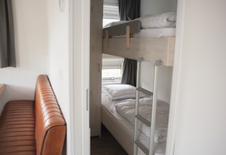 Indretning af et soveområde med køjesenge og en brun læderbænk i Veluwelodge XL, De Boshoek, Holland.