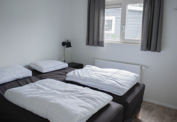 Chambre à Veluwelodge XL au Holiday park De Boshoek, Pays-Bas, deux lits simples, fenêtre et rideaux.