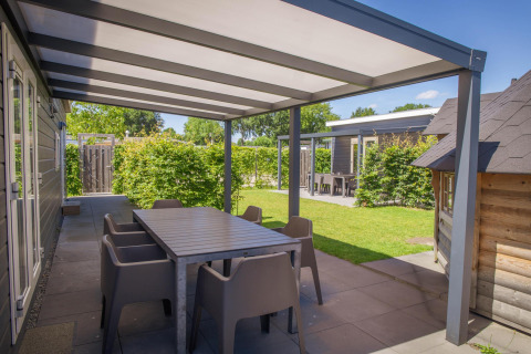 Udendørs terrasse med overdækning og spisebord ved Veluwelodge XL på Holiday park De Boshoek i Holland.