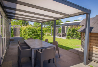 Udendørs terrasse med overdækning og spisebord ved Veluwelodge XL på Holiday park De Boshoek i Holland.