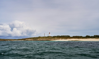 Vista sobre el mar hacia una costa con un faro en un parque vacacional que ofrece alojamiento glamping.
