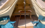 Binnenzicht op een safaritent met twee kampeerstoelen vooraan, een dubbel bed en een houten tafeltje.