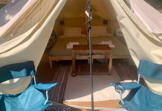 Binnenzicht op een safaritent met twee kampeerstoelen vooraan, een dubbel bed en een houten tafeltje.