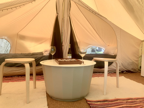Sfeervol safaritent-interieur met twee bedden, ronde tafel, twee krukken, wijnfles en glazen.