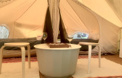 Interno di tenda safari con due letti, tavolino rotondo, due sgabelli, bottiglia di vino e bicchieri.