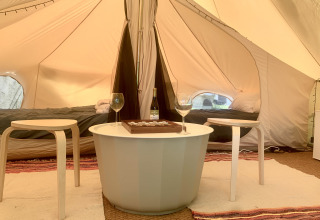 Safari-Zelt-Inneneinrichtung mit zwei Betten, kleinem Tisch, zwei Hockern, Weinflasche und Gläsern.