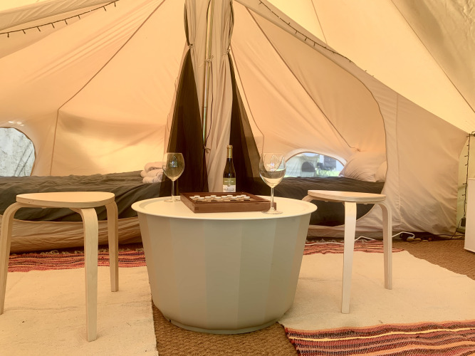 Sfeervol safaritent-interieur met twee bedden, ronde tafel, twee krukken, wijnfles en glazen.