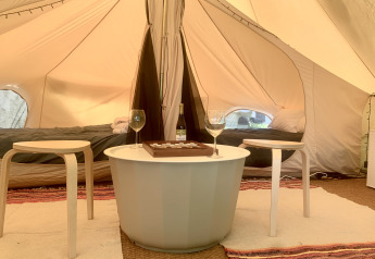 Sfeervol safaritent-interieur met twee bedden, ronde tafel, twee krukken, wijnfles en glazen.