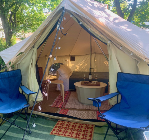 Binnenzicht van Carvalho 4 Meter XL Bell Tent met blauwe stoelen, tapijten en gezellige verlichting.