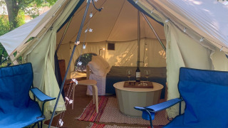 Binnenzicht van Carvalho 4 Meter XL Bell Tent met blauwe stoelen, tapijten en gezellige verlichting.