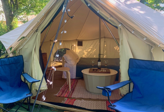 Binnenzicht van Carvalho 4 Meter XL Bell Tent met blauwe stoelen, tapijten en gezellige verlichting.