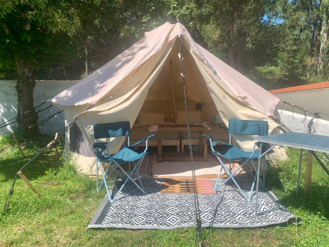 Safaritent met open deur, twee blauwe kampeerstoelen en een tafel op een tapijt in het gras.