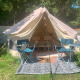 Safari-telt med åbent telt, to campingstole, et bord og tæppe på græsset under træer i solen.