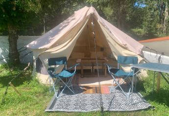 Safaritent met open deur, twee blauwe kampeerstoelen en een tafel op een tapijt in het gras.