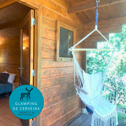 Cabaña Azalea en Glamping de Cerveira, Portugal, con silla colgante en el porche y espacio interior acogedor.