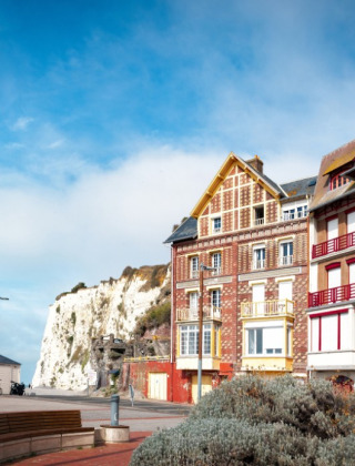 Maisons colorées en bord de mer, falaise blanche et promenade agréable sous un ciel bleu lumineux.