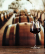 Un verre de vin rouge et des bouteilles sur une table en bois, avec des fûts en arrière-plan près de Wissignicourt, Canaries.