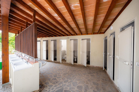 Outdoor communal toilets and sinks at Villatent Wood, Camping Casa dei Prati, Italy, under wooden beams.