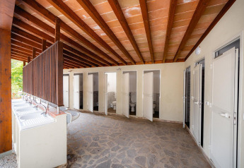 Outdoor communal toilets and sinks at Villatent Wood, Camping Casa dei Prati, Italy, under wooden beams.