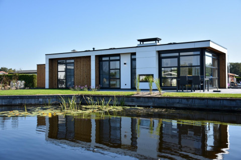 Lodge moderno con ventanales y detalles de madera, reflejado en un estanque bajo un cielo despejado.